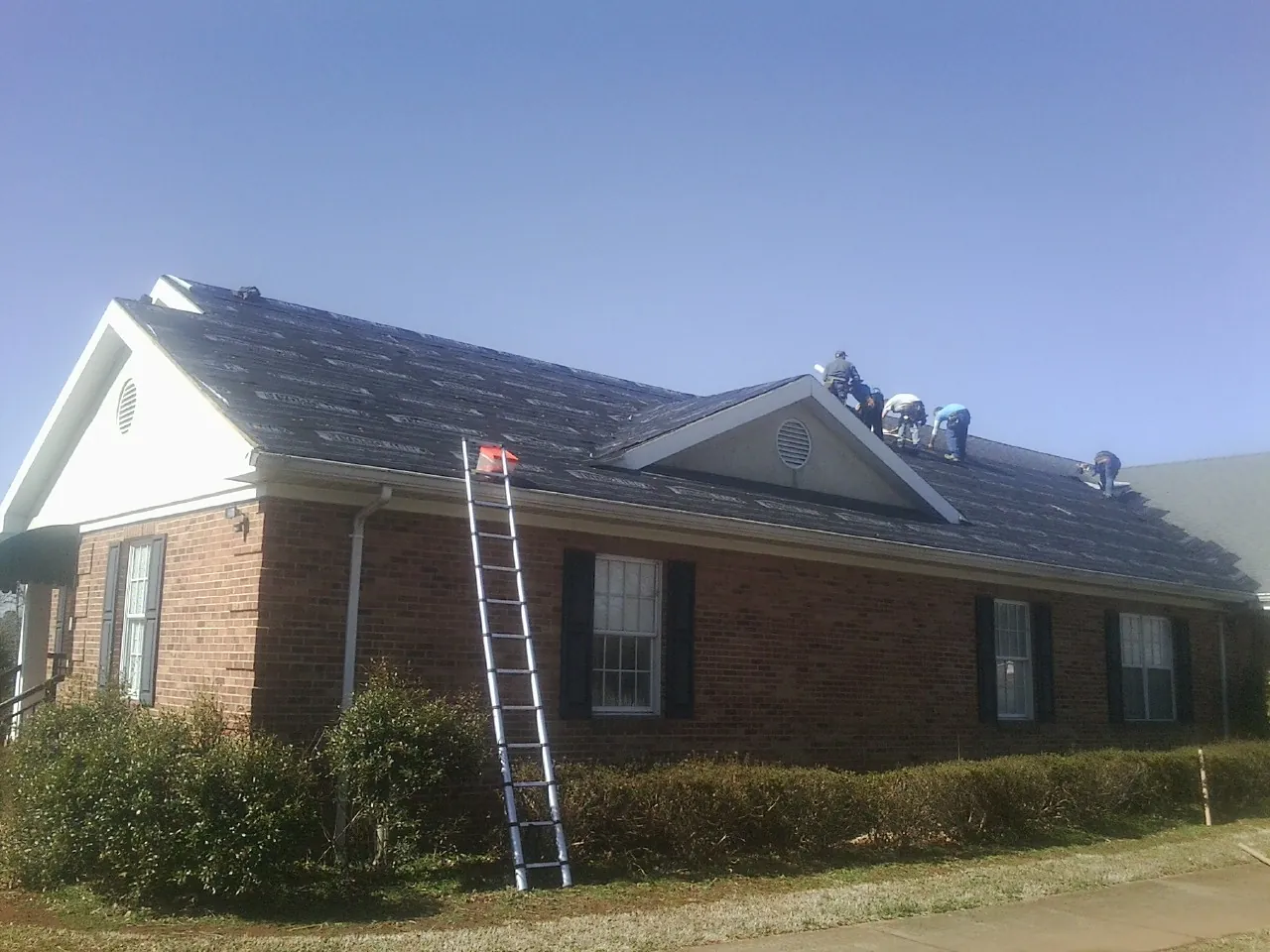 Crew tearing shingles off a brick ranch roof with a ladder set — Metal Roof Repair work by our crew in Tilghman