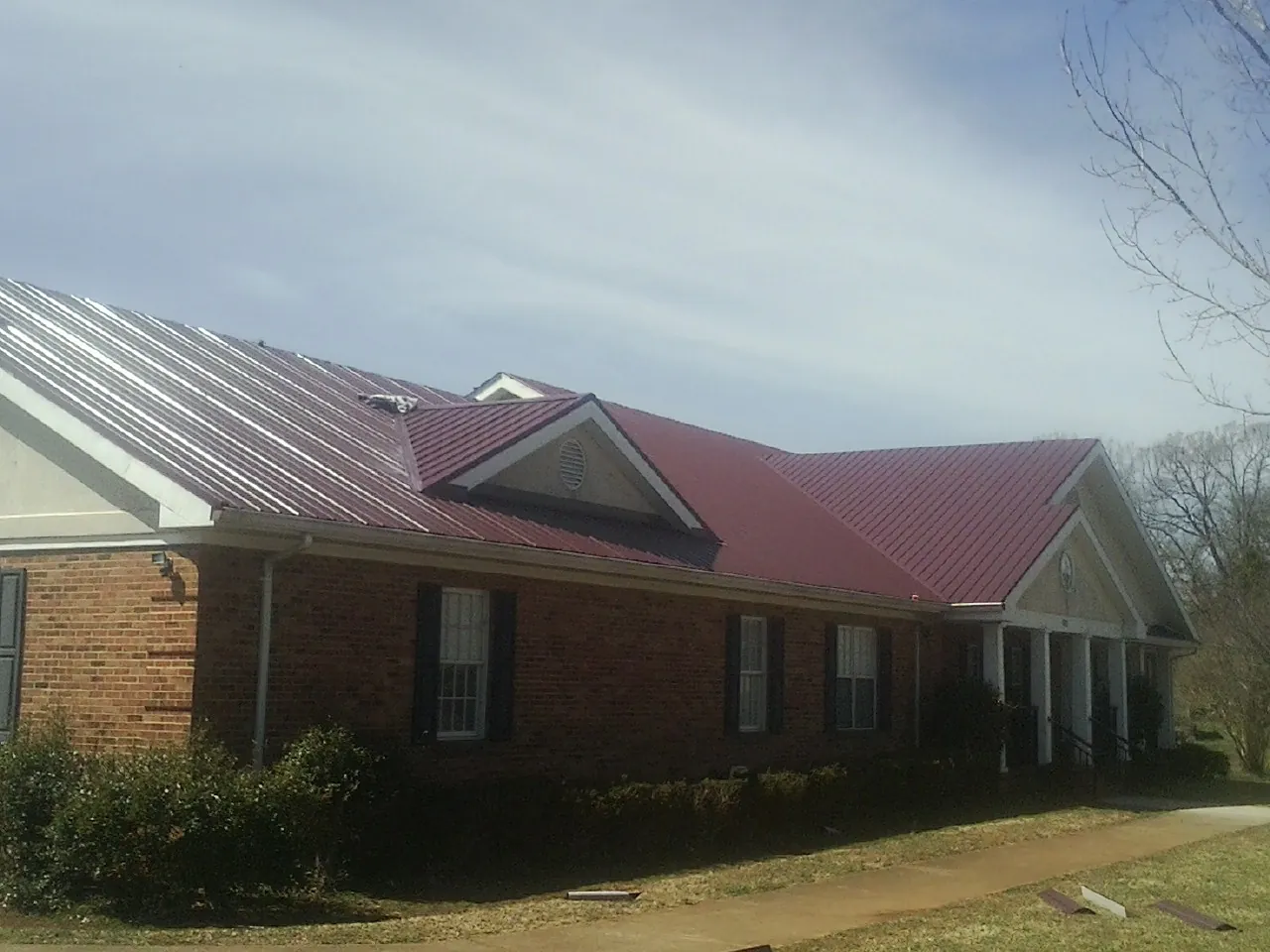 Red metal roof with gabled entries on a long brick building, from a Hail Damage Roof Repair job in Tilghman