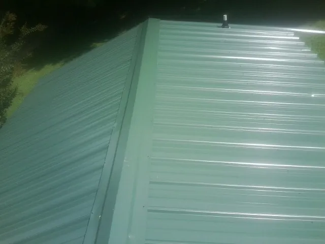 New green metal panels meeting at the ridge of a roof — Flat Roof Repair work by our crew in Tilghman